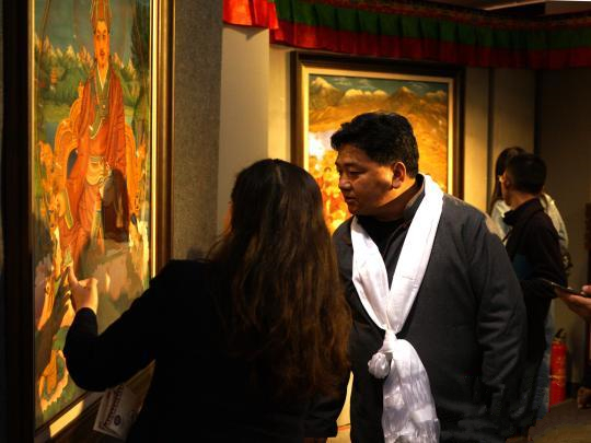 西藏安多强巴唐卡艺术画院负责人边巴次仁(系白色哈达者)，在展览现场向大家介绍他们的唐卡作品。