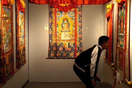 安多强巴唐卡艺术画院作品风格有别于西藏其他传统唐卡画派。图为11日展览现场，一位参观者仔细端详一幅唐卡作品。